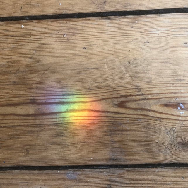 Ein Lichtpunkt in Regenbogen Farben auf einem Hintergrund aus Holz.